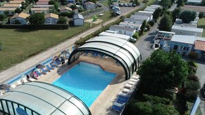 Una piscina con sillones de descanso y sombrillas, rodeada por una zona techada con techo curvo.