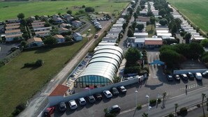 Vista aérea de una zona residencial con casas, un edificio grande y curvo, y un estacionamiento.