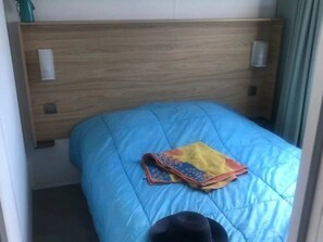 Uma cama pequena e bem arrumada, com um edredom azul e um cobertor colorido.