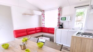 Cocina compacta con microondas, estufa y lavamanos. Hay un comedor con mesa y sillas, y un sofá rojo.