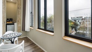 A modern room with large windows, a small table, and a kitchenette area. - GuestReady - Alegria 293 - Room 4 (Porto)