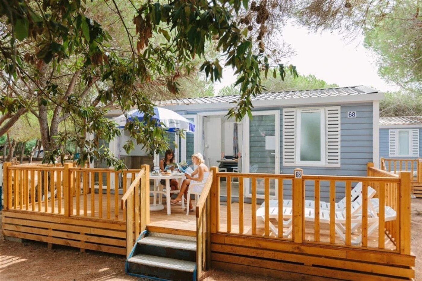 A wooden deck with a table and chairs, a covered outdoor area, and a mobile home with the number 68.