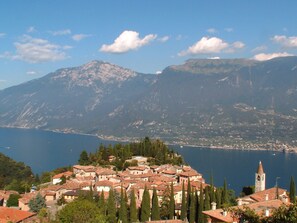 A coastal village with terracotta-roofed buildings, a prominent church tower, and a mountain range in the background.