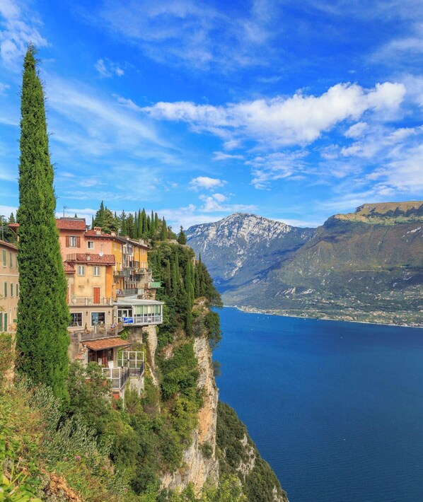 A coastal building with balconies overlooking a lake, surrounded by greenery and mountains.
