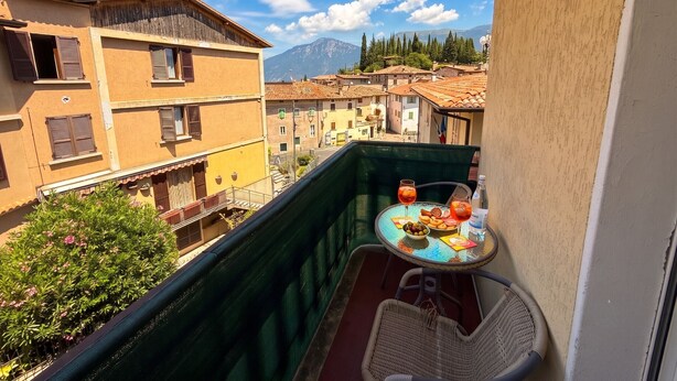 A balcony with a table set for two, overlooking a town with traditional architecture and a mountain in the background. - Casa Liver Pieve balcony town center (Tremosine)