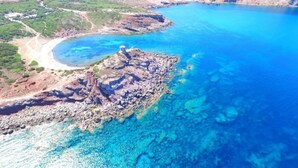 An aerial view of a coastal area with clear blue waters, rocky terrain, and a winding road.