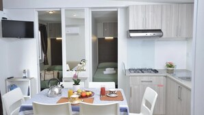 A compact hotel room with a dining area, kitchenette, and a bed visible through a sliding door.