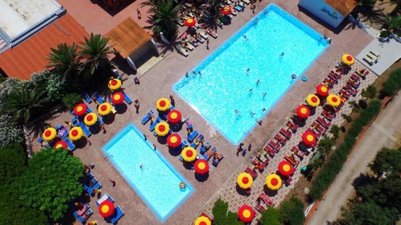 Vue aérienne d’un espace piscine comprenant deux piscines, entourées de transats et de parasols.