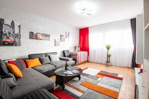 Un salon moderne avec un canapé gris, une table basse et un coin repas agrémenté d’une nappe rouge.