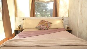 A bed with a beige blanket, a pink throw, and a decorative pillow. There are two bedside tables with candles and a window with curtains. - ZEcamping 4 étoiles animé pataugeoire dog friendly locatif clim 40m2 (Alghero)