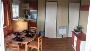 A compact kitchen with a dining area, wooden flooring, and a small potted plant. - ZEcamping 4 étoiles animaux acceptés tennis pataugeoire (Tamniès)