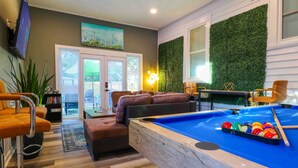 A modern living room with a pool table, comfortable seating, and a green wall. - Fun hangout; Perfect Location; Walk to Coliseum (Greensboro)