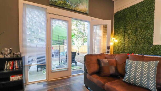 A living room with a brown leather sofa, a bookshelf, and a green wall. - Fun hangout; Perfect Location; Walk to Coliseum (Greensboro)