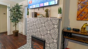 A living room with a fireplace, a flat-screen TV mounted above it, and a potted plant to the left. - Fun hangout; Perfect Location; Walk to Coliseum (Greensboro)