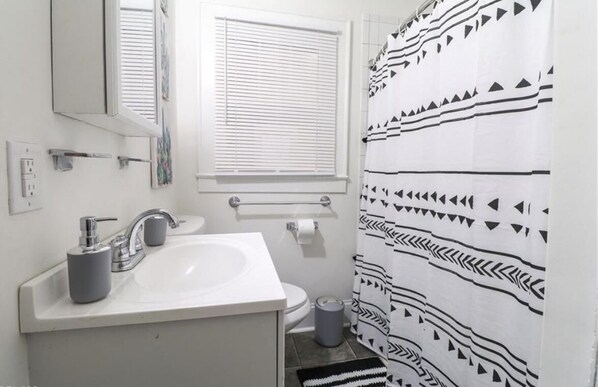 Un baño con lavamanos blanco, espejo y ventana con persianas.