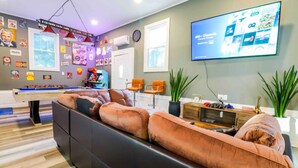 A modern living room with a pool table, comfortable seating, a flat-screen TV, and various wall decorations. - Fun hangout; Perfect Location; Walk to Coliseum (Greensboro)