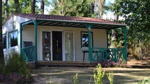 Ein kleines, eingeschossiges Gebäude mit einer Veranda, umgeben von einem Garten mit verschiedenen Pflanzen.