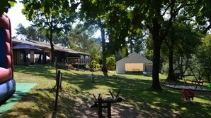 Ein Park mit einem Spielplatz, einem überdachten Picknickbereich und einem Gebäude mit einer Terrasse.