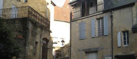 A cobblestone courtyard with a statue of two birds, surrounded by historic buildings with stone facades and traditional architecture.