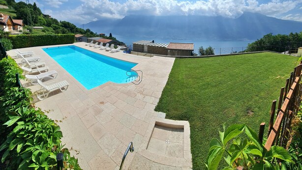 Una piscina con sillones de descanso, zona verde y vistas a un lago y montañas.