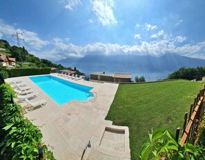 Une piscine avec des chaises longues, une pelouse et une vue sur un lac et des montagnes.