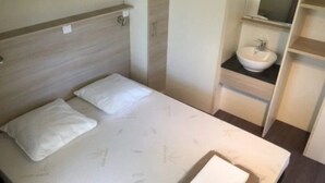 Een slaapkamer met een bed, nachtkastje, inbouwplank en een badkamer met wastafel en spiegel.
