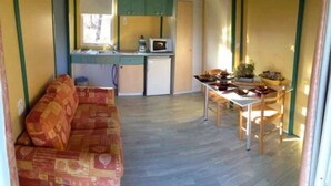 A compact living space with a sofa, a dining table with chairs, a small kitchenette with a microwave, and a window allowing natural light. - ZEcamping 4 étoiles pataugeoire piscine chiens acceptés chalet TV 40m2 (Tamniès)
