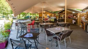 An outdoor cafe with wooden tables and chairs, a covered seating area, and a bar.