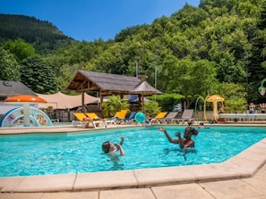 Une piscine avec des chaises longues, un espace ombragé et une vue sur les montagnes en arrière-plan.