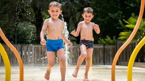 Two children playing in a water feature with a wooden fence and greenery in the background.