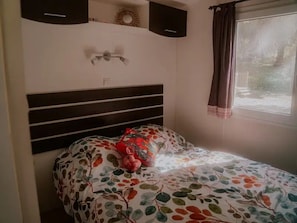 Un dormitorio con cama, cabecera, ventana con cortinas y lámpara de pared.