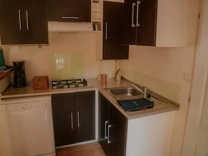 A compact kitchen with dark cabinets, a gas stove, a sink, and a dishwasher. - ZEcamping 3 étoiles familial piscine chauffée dog friendly locatif TV LV clim (Florac)