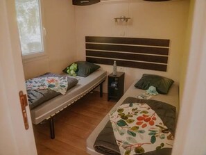 A compact room with two single beds, a small table, and a window. - ZEcamping 3 étoiles familial piscine chauffée dog friendly locatif TV LV clim (Florac)