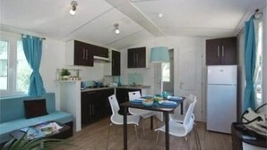 A compact kitchen with dark cabinets, a white refrigerator, and a dining table with chairs. - ZEcamping 3* familial piscine chauffée dog friendly locatif TV LV clim (Florac)