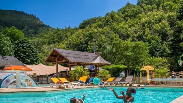 Una piscina con sillones de descanso y una zona sombreada.