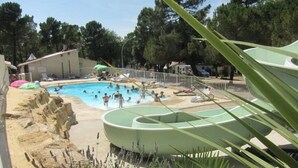 A pool area with a water slide, surrounded by a sandy beach and some vegetation.