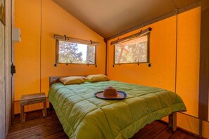 Een kamer met een enkel bed, een klein houten krukje en twee ramen met gordijnen.