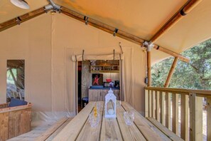 Een houten terras met een tafel en stoelen, een houten leuning, en uitzicht op een keuken met een aanrecht en kasten.