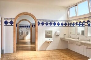 Ein Badezimmer mit gefliestem Boden, einem Waschbeckenbereich mit Spiegeln und einer Urinenschale.