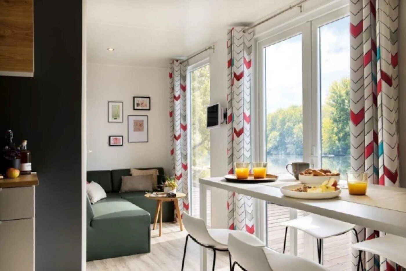 A modern room with a green sofa, a dining table with breakfast items, and large windows with chevron-patterned curtains.