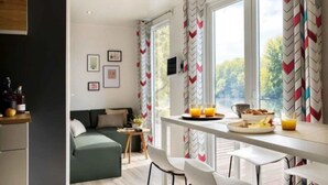 A modern room with a green sofa, a dining table with breakfast items, and large windows with chevron-patterned curtains. - ZEcamping 4 étoiles piscine dog friendly club enfant mobil-home TV LV clim (Pals)