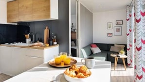 A modern kitchen with a wooden cabinet, a dining table with breakfast items, and a cozy living area with a sofa and a coffee table. - ZEcamping 4 étoiles piscine dog friendly club enfant mobil-home TV LV clim (Pals)