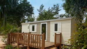Une maison mobile de plain-pied avec une terrasse en bois, une porte d’entrée et une petite fenêtre.