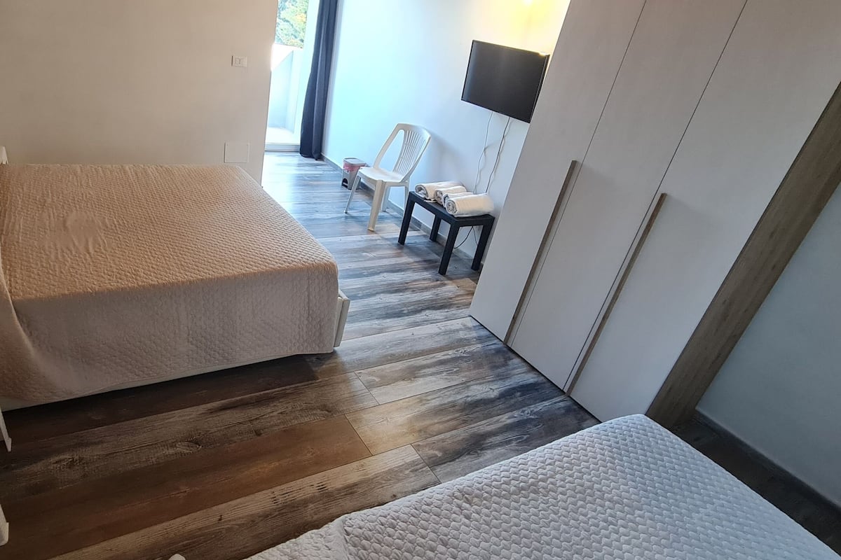 Une chambre à coucher de taille réduite, comprenant un lit, une petite table de chevet, un téléviseur fixé au mur et une chaise.