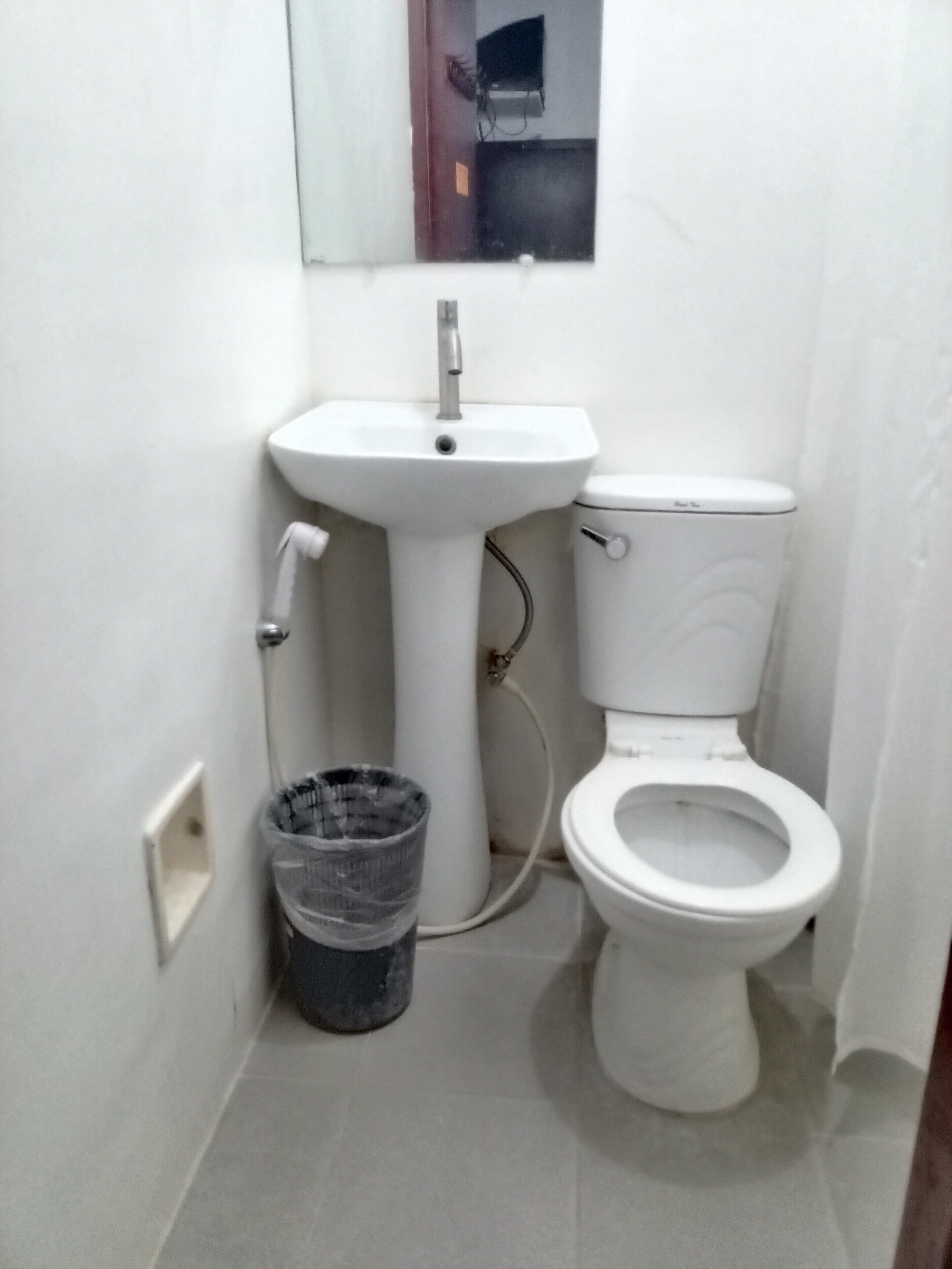 A small, white bathroom with a pedestal sink, toilet, and a trash bin.