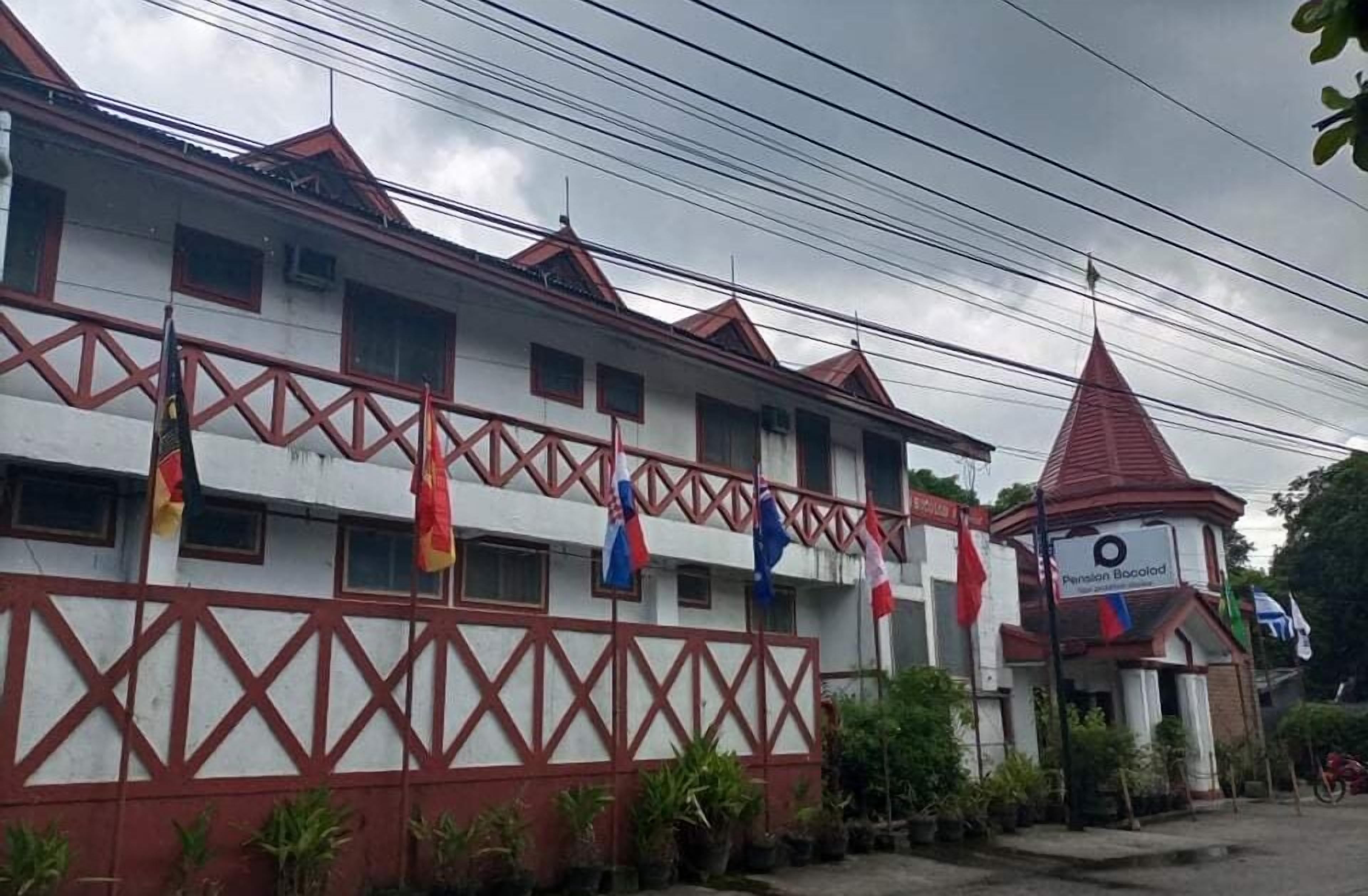 A building with a red and white facade, multiple windows, and a red-roofed tower. Flags are hanging on the exterior.