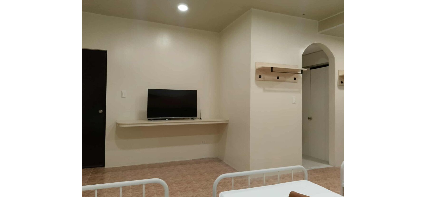 A room with a television on a shelf, a door, and a white bed.