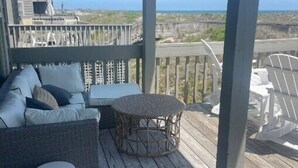 Een overdekt terras met een bank, poef en stoelen, met uitzicht op een strand.