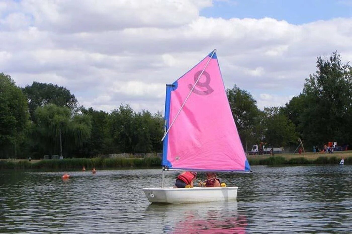 En sejlbåd med et pink sejl på en rolig sø omgivet af træer.