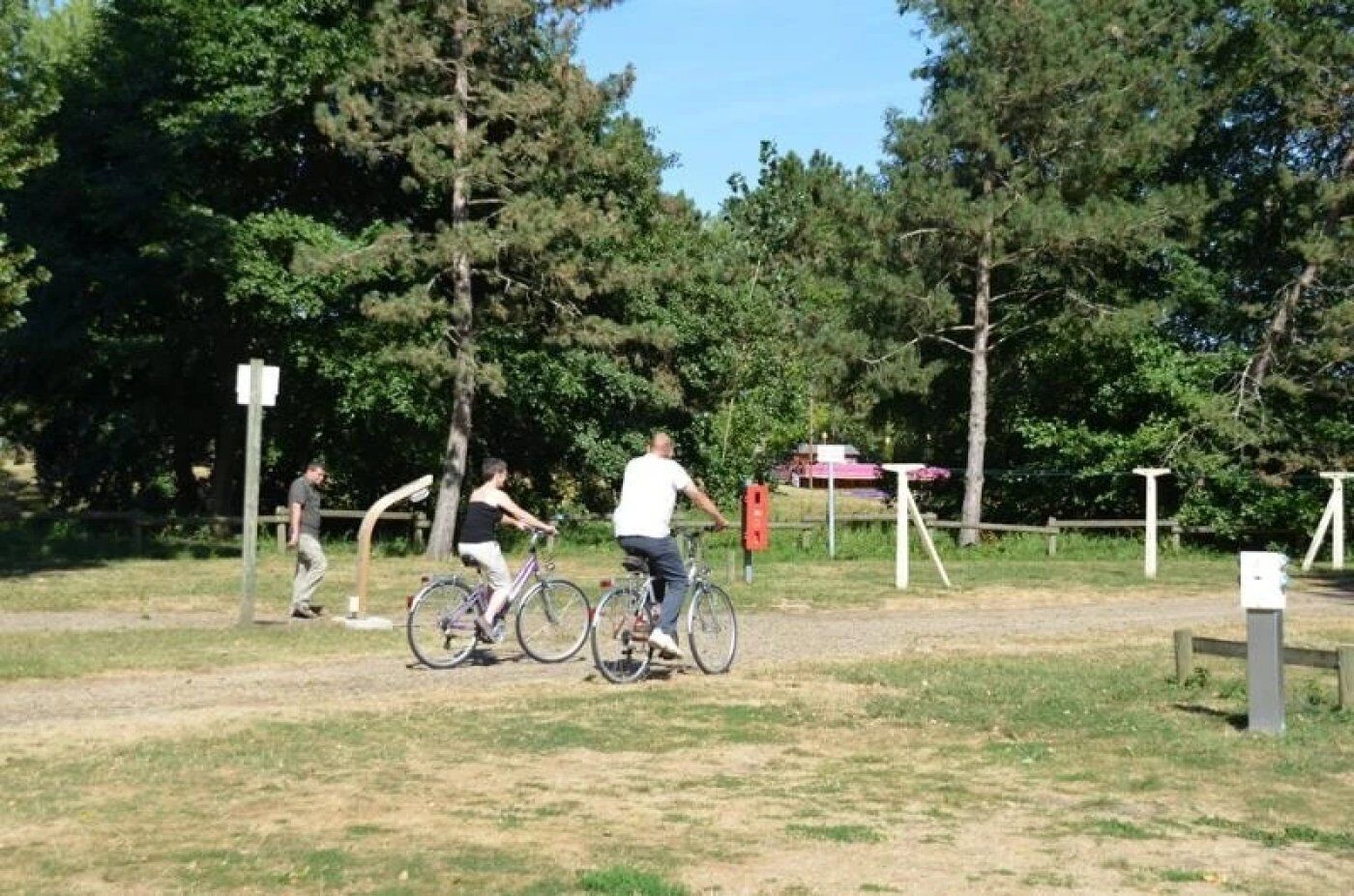 A park with a dirt path, bicycles, and people riding bikes.